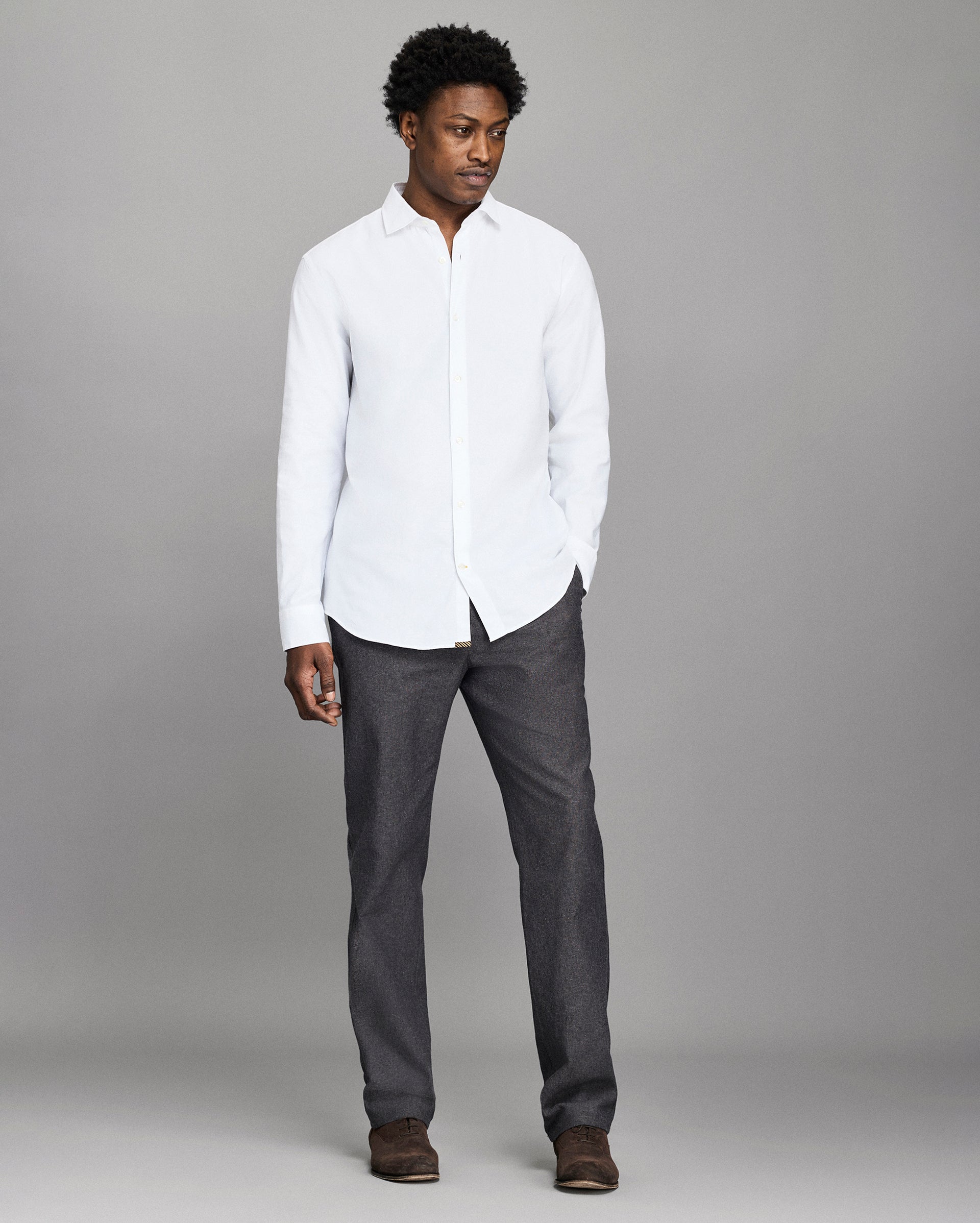 Man wearing a white shirt and dark pants against a gray background
