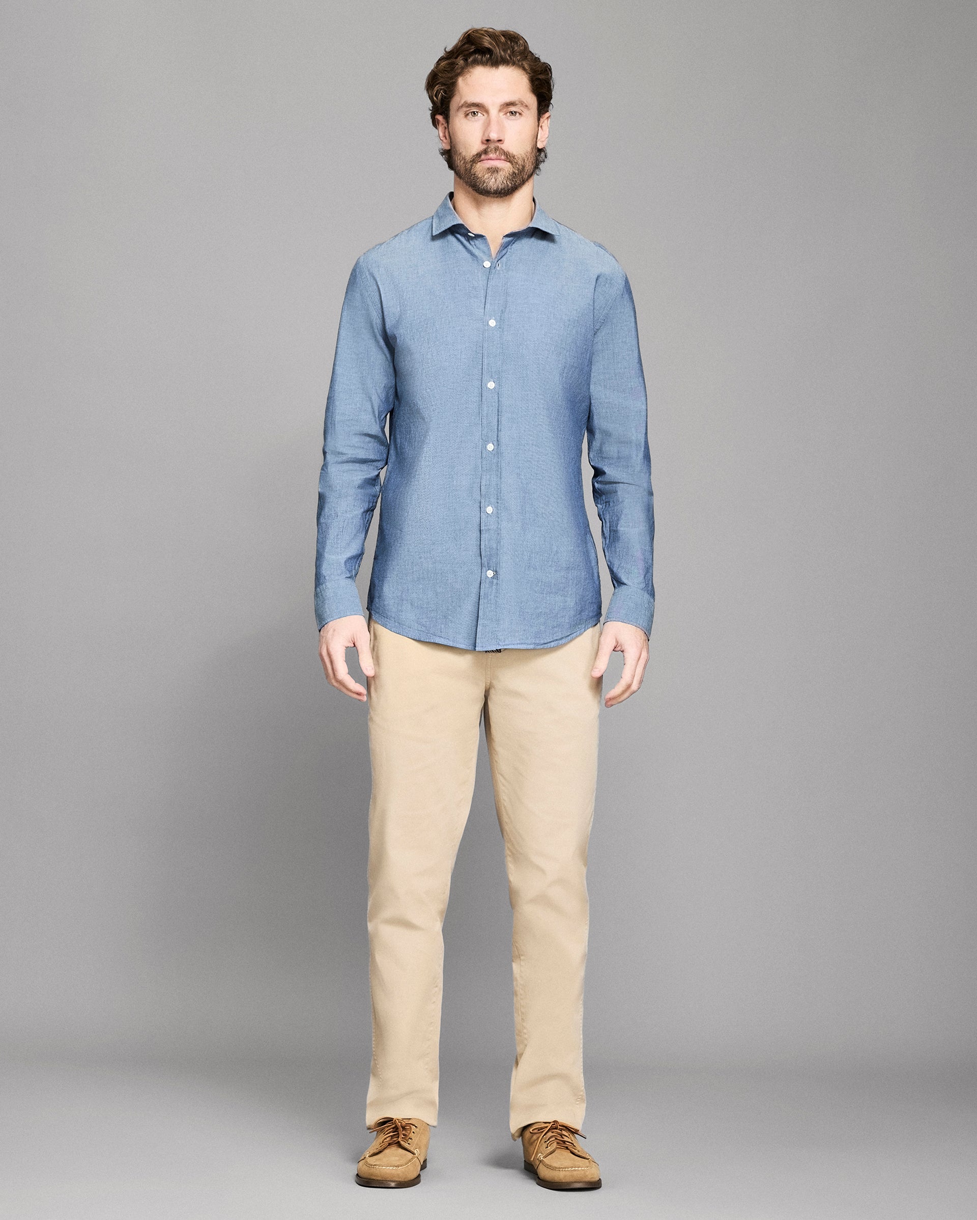 Man wearing a blue shirt and beige pants on a gray background
