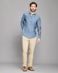 Man wearing a blue shirt and beige pants against a gray background