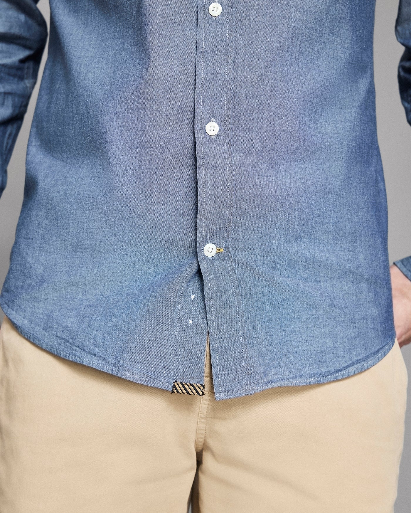 Close-up of a person wearing a blue button-up shirt and beige pants.