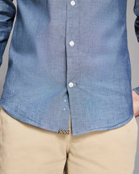 Close-up of a person wearing a blue button-up shirt and beige pants.