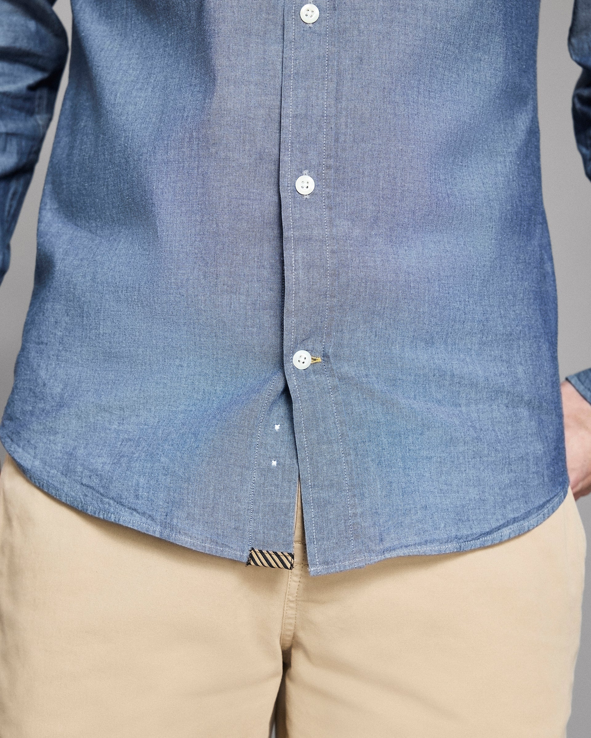 Close-up of a person wearing a blue button-up shirt and beige pants.