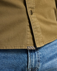 Close-up of a brown shirt collar and blue jeans with a brand label.