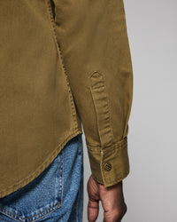 Close-up of a person wearing a green jacket with rolled-up sleeve and blue jeans on a gray background