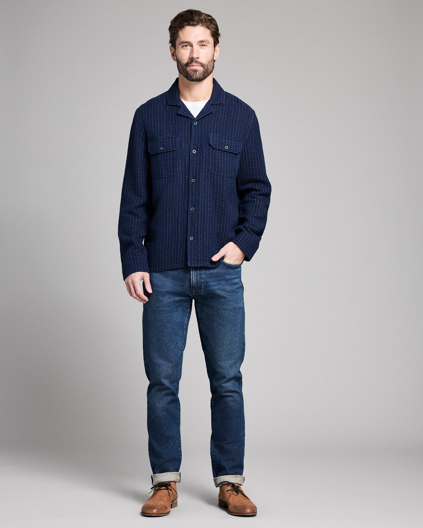 Man wearing a navy blue textured shirt and jeans on a gray background