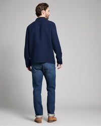 Man wearing a navy ribbed sweater and blue jeans on a gray background