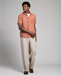 Man wearing a patterned shirt and beige pants on a gray background