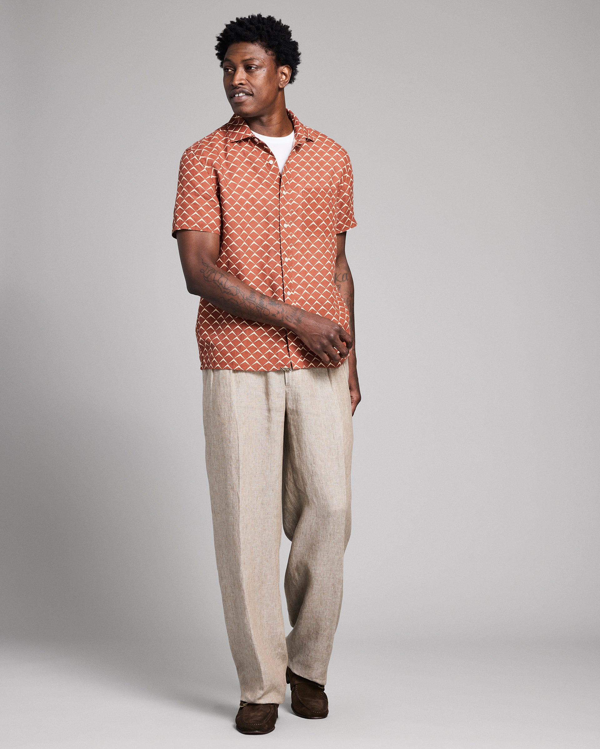 Man wearing a patterned shirt and beige pants on a gray background