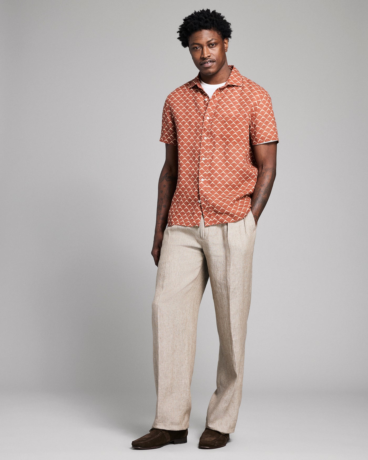 Man wearing a patterned shirt and beige pants on a gray background