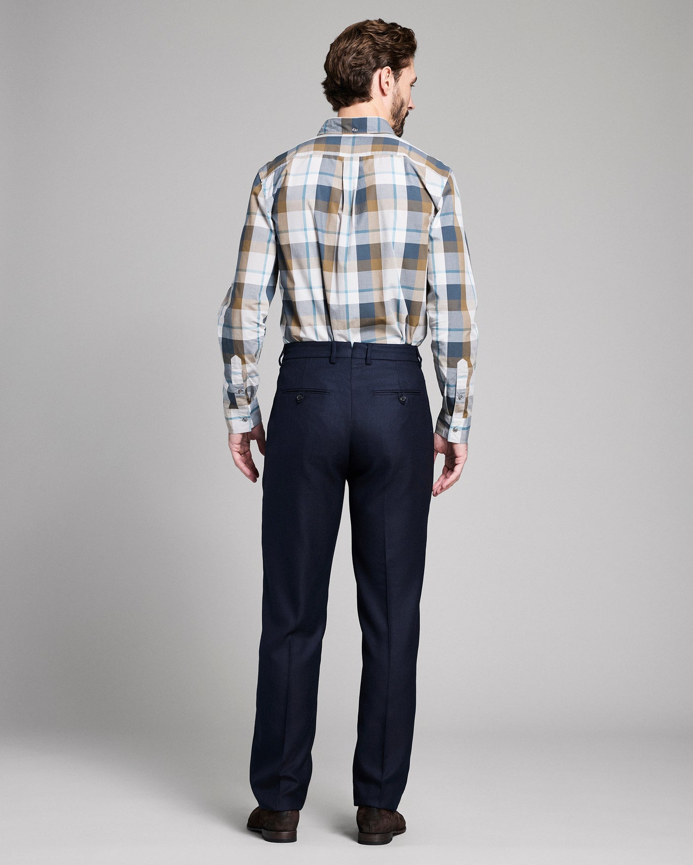 Man wearing a plaid shirt and dark pants on a gray background