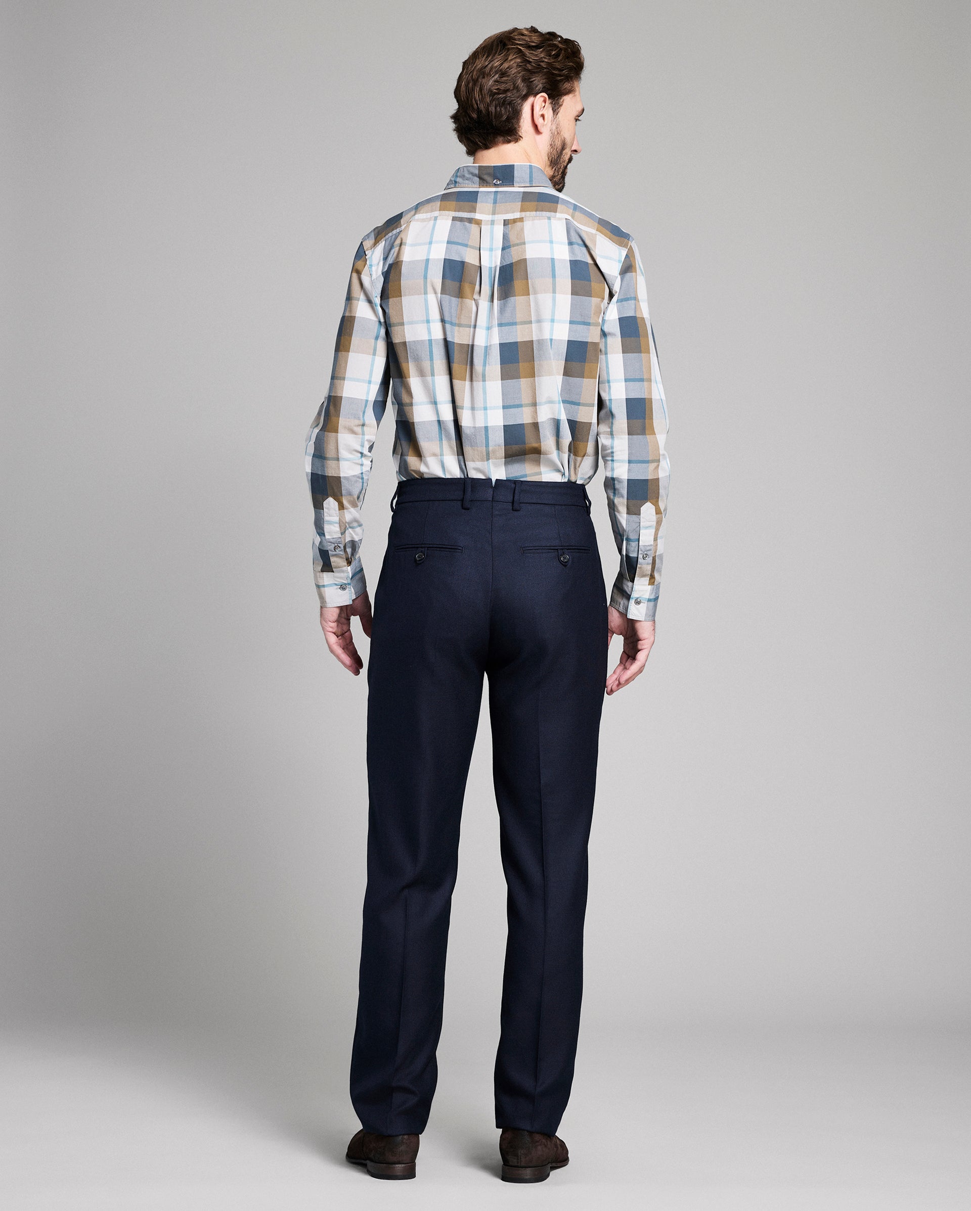 Man wearing a plaid shirt and dark pants on a gray background