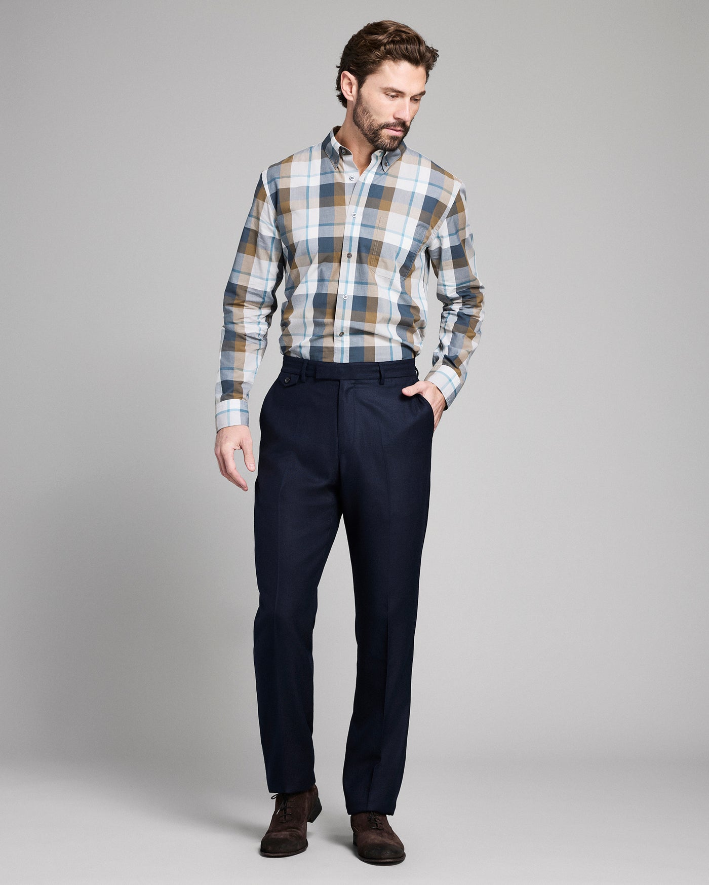 Man wearing a plaid shirt and dark pants on a gray background