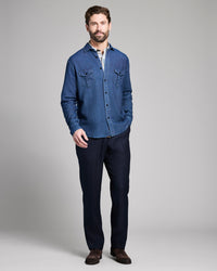 Man wearing a blue denim shirt and dark pants on a gray background