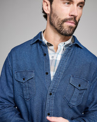 Man wearing a blue denim shirt over a checkered shirt against a gray background