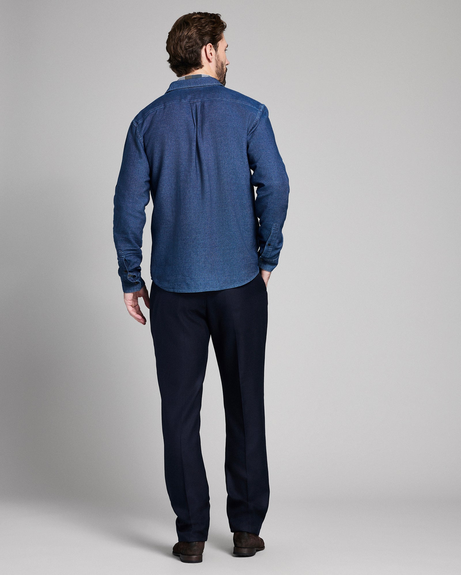 Man wearing a blue shirt and dark pants on a gray background