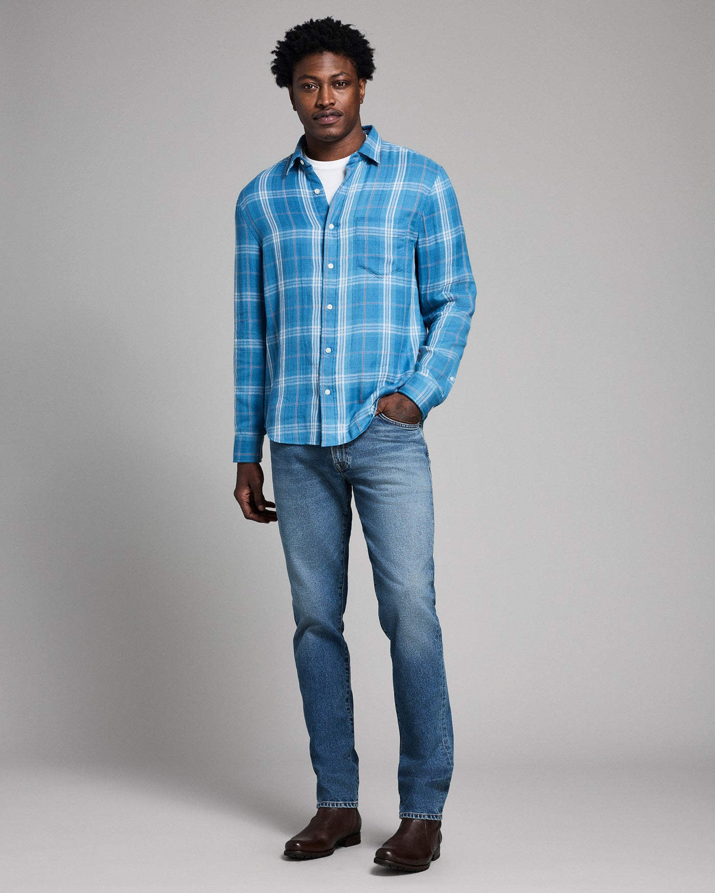 Man wearing a blue plaid shirt and jeans on a gray background