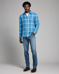 Man wearing a blue plaid shirt and jeans on a gray background