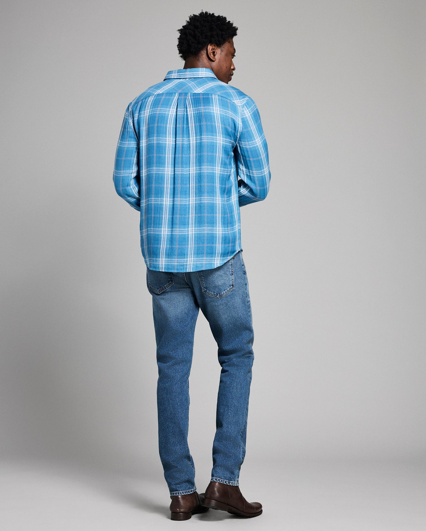 Person wearing a blue plaid shirt and jeans on a gray background