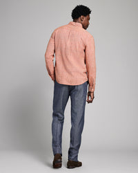 Man wearing a orange checkered shirt and blue jeans against a gray background