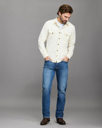 Man wearing a light-colored denim jacket and blue jeans on a gray background