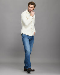Man wearing a white shirt and blue jeans against a gray background
