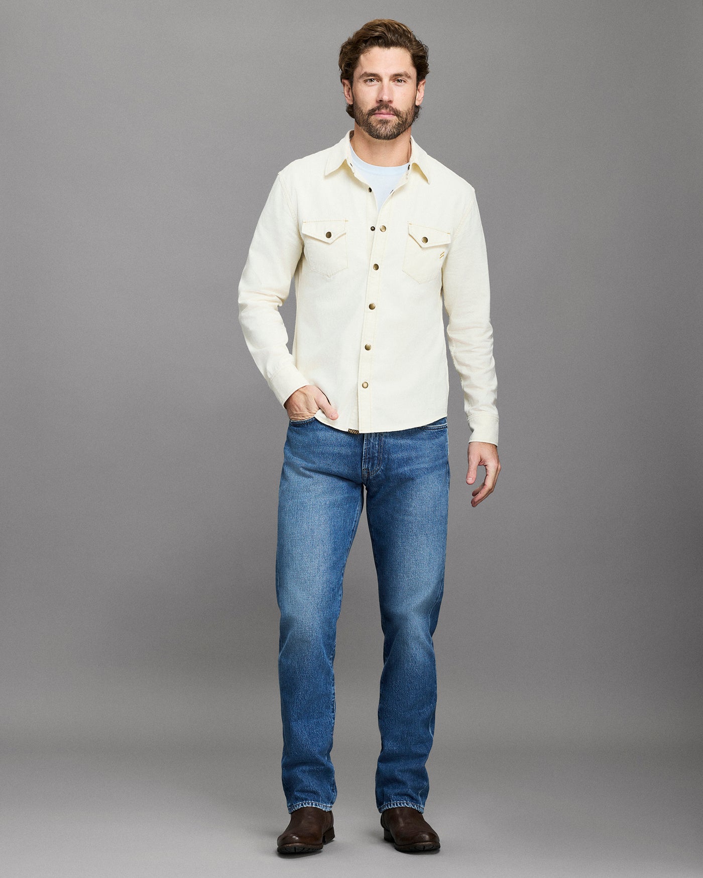 Man wearing a white shirt and blue jeans against a gray background
