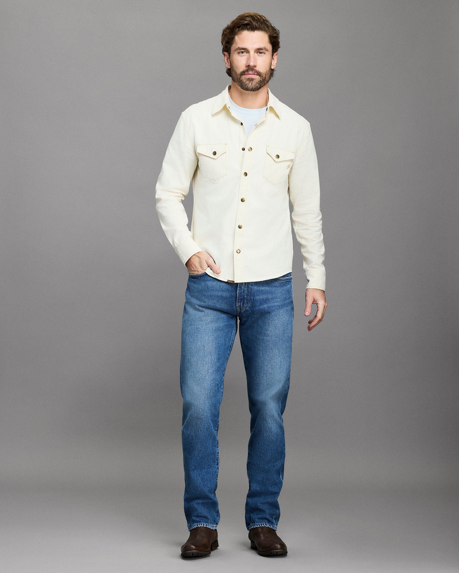 Man wearing a white shirt and blue jeans against a gray background