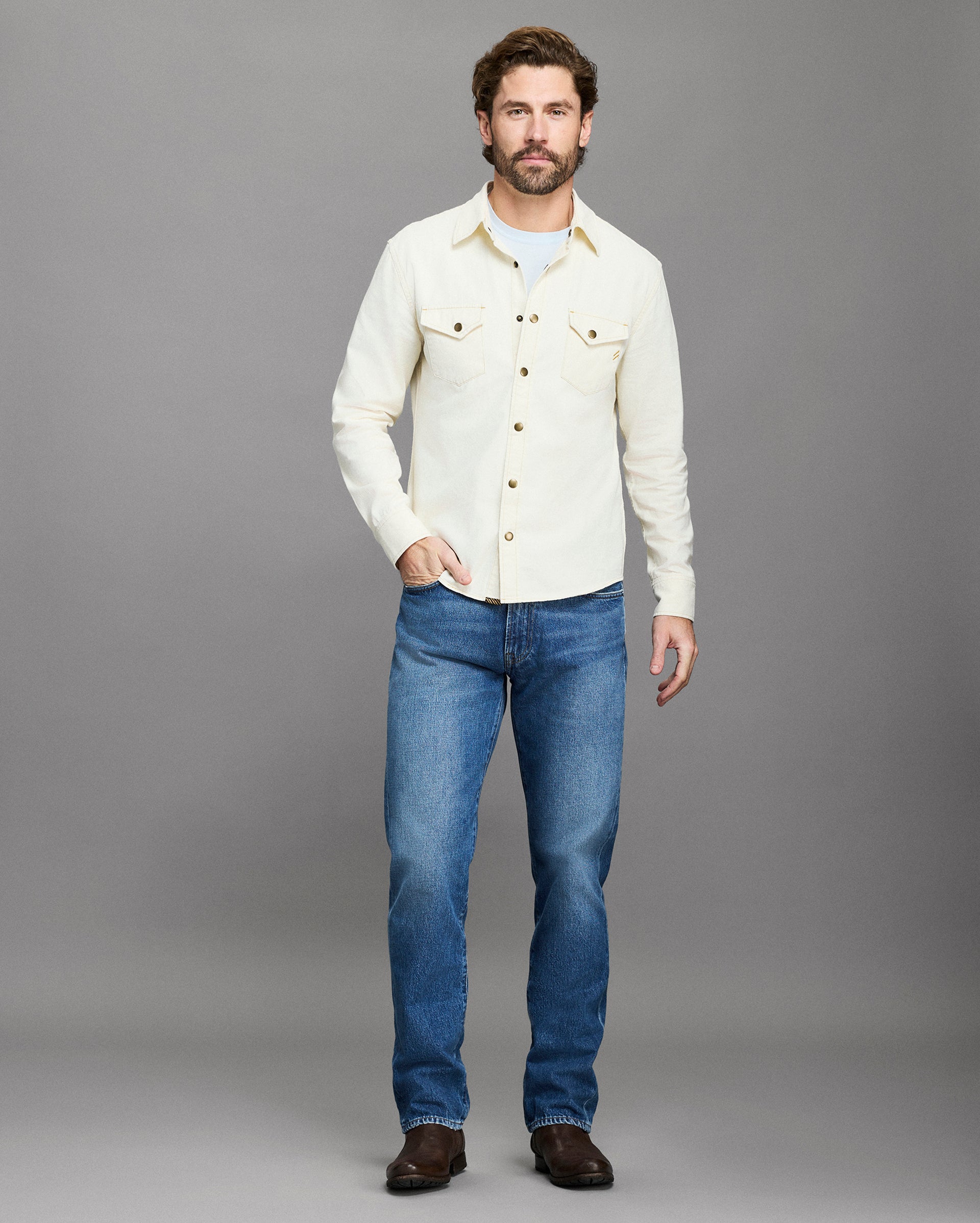 Man wearing a white shirt and blue jeans against a gray background