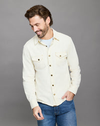 Man wearing a cream denim jacket and blue jeans on a gray background
