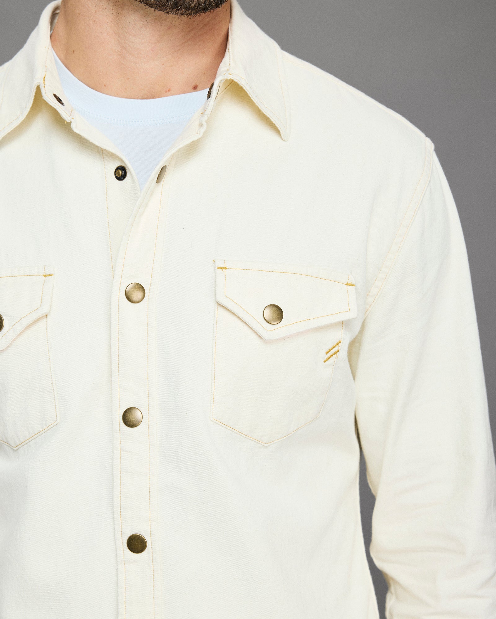 Close-up of a cream-colored denim shirt with button details on a gray background