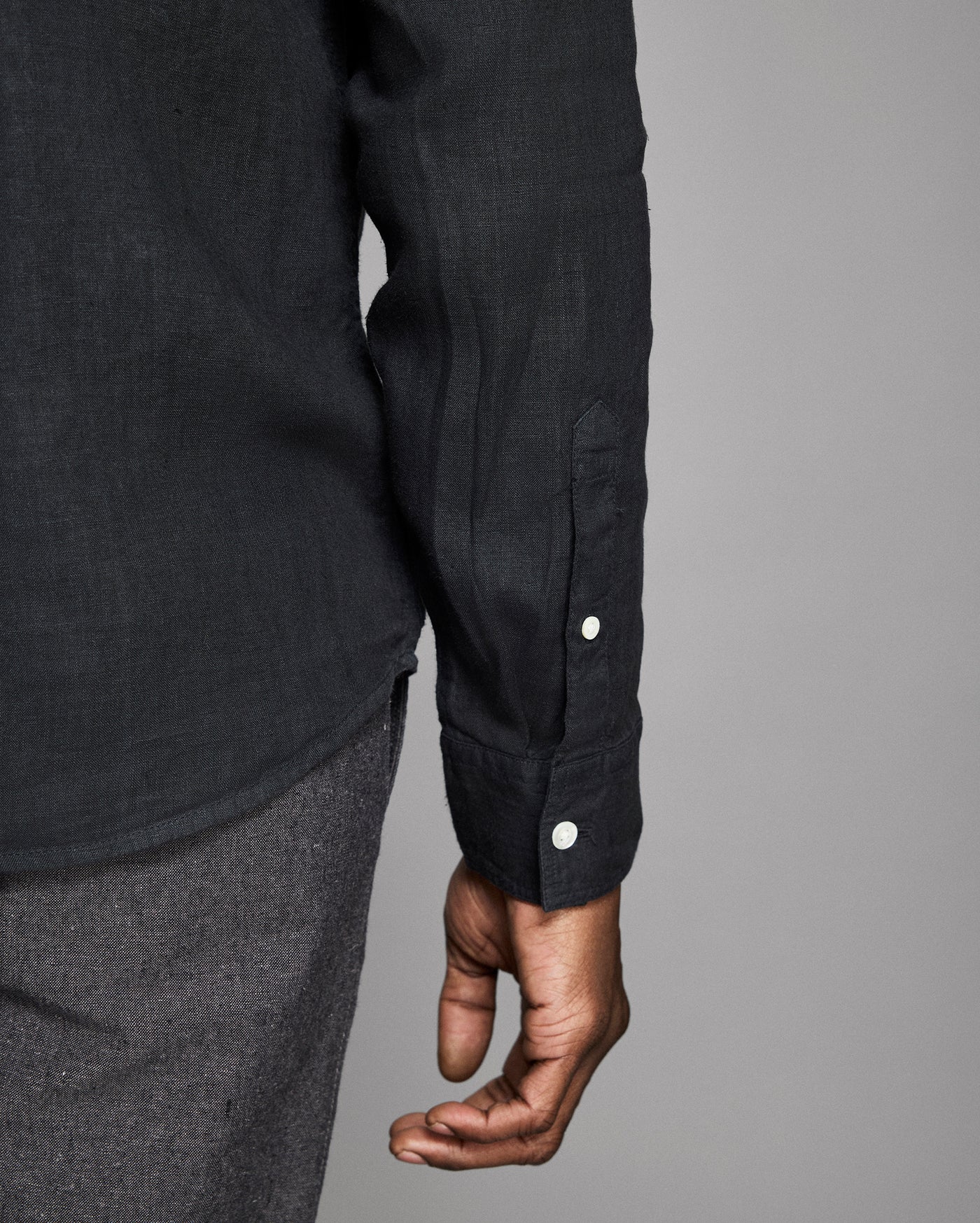 Close-up of a person wearing a black shirt with button details on a gray background