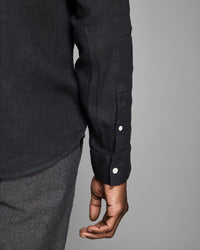 Close-up of a person wearing a black shirt with button details on a gray background