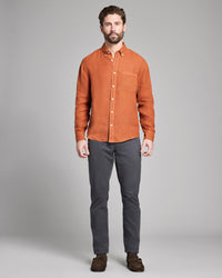 Man wearing an orange button-up shirt and gray pants against a plain background
