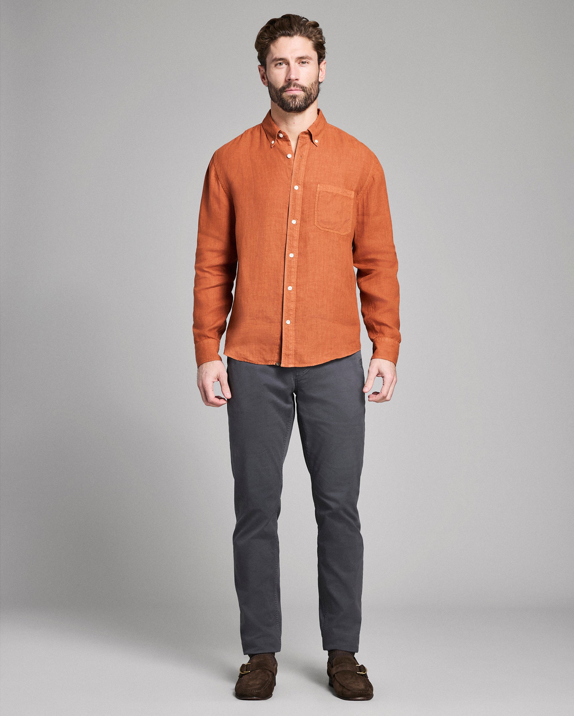 Man wearing an orange button-up shirt and gray pants against a plain background