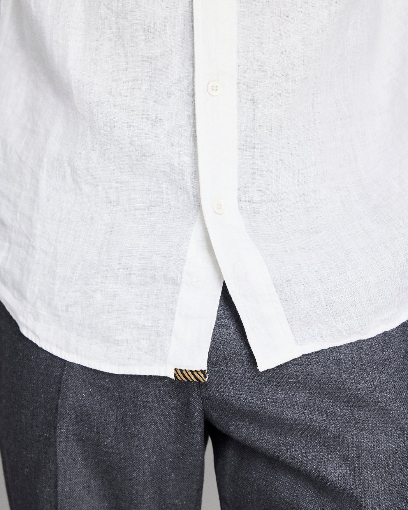 Close-up of a white shirt with a collar and gray pants on a light gray background