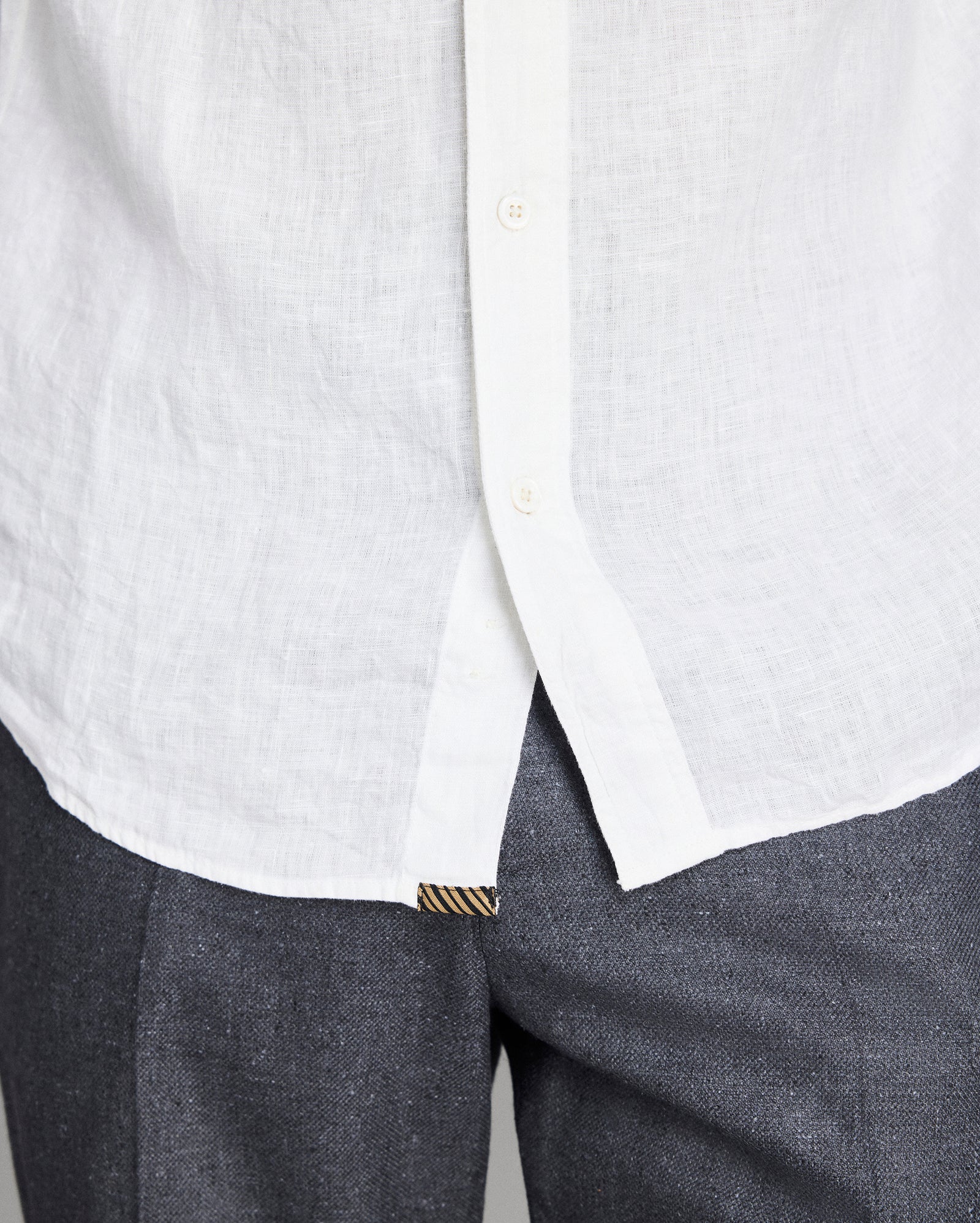 Close-up of a white shirt with a collar and gray pants on a light gray background