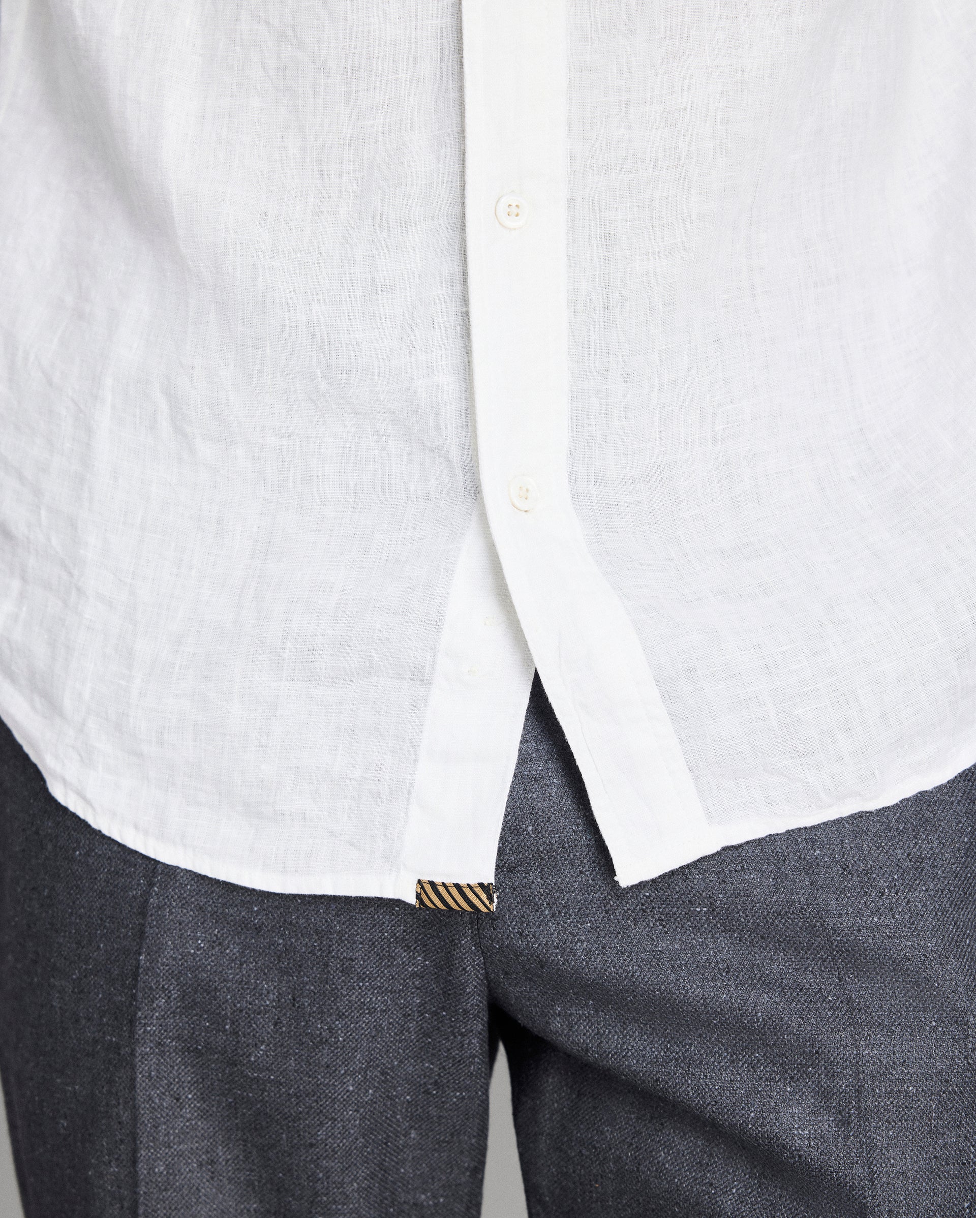 Close-up of a white shirt with a collar and gray pants on a light gray background