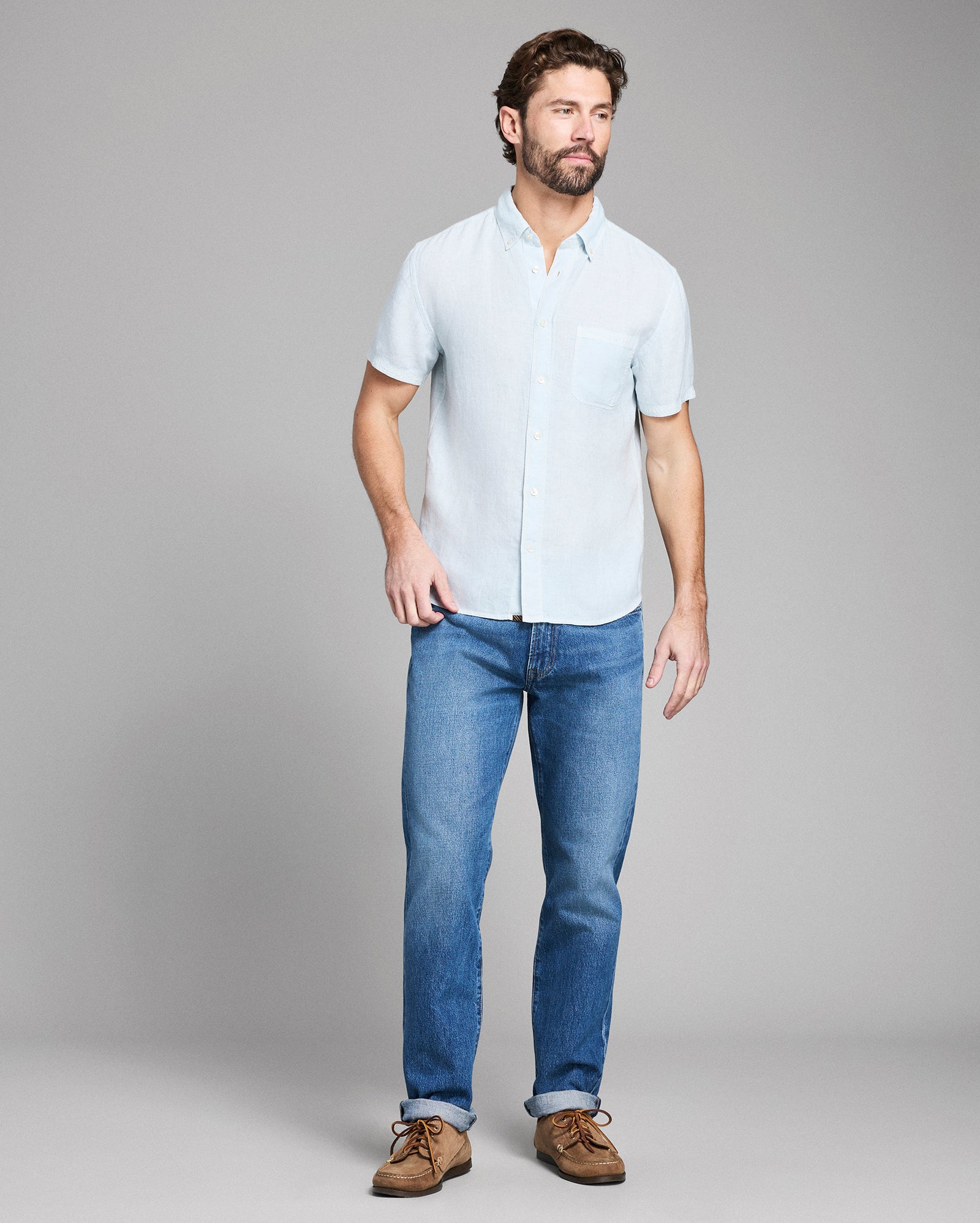 Man wearing a light blue shirt and jeans on a gray background