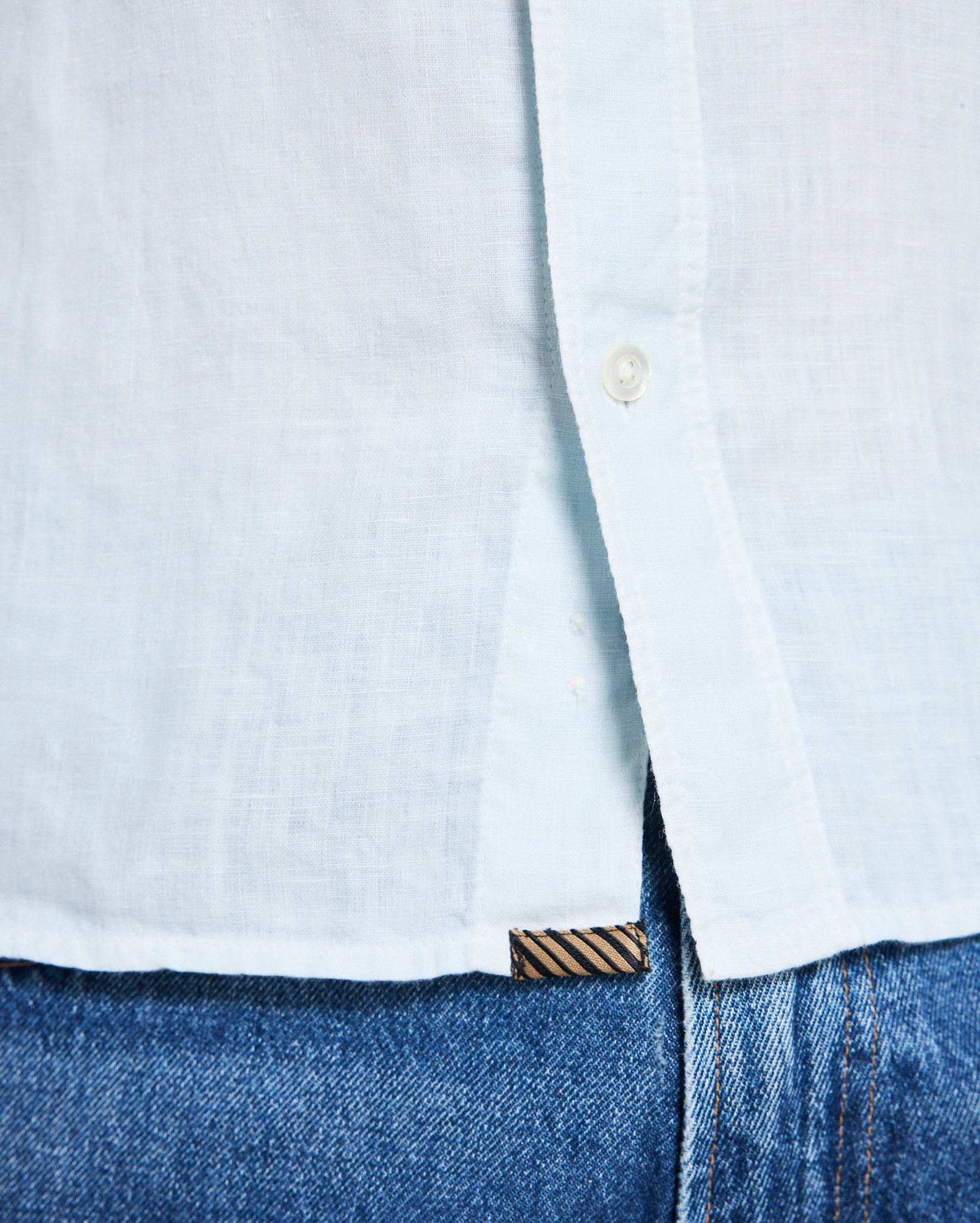 Close-up of a light blue button-up shirt and blue jeans with a brand logo.