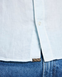 Close-up of a light blue button-up shirt and blue jeans with a brand logo.