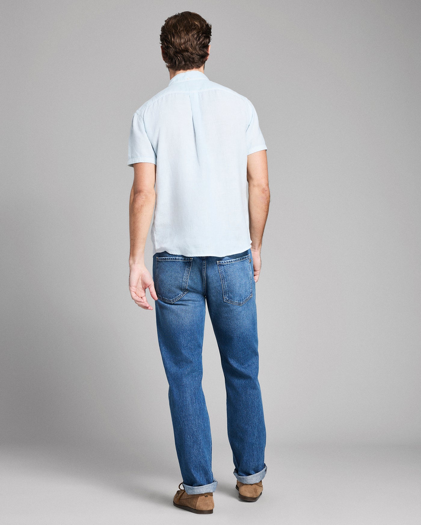 Man wearing a white shirt and blue jeans on a gray background