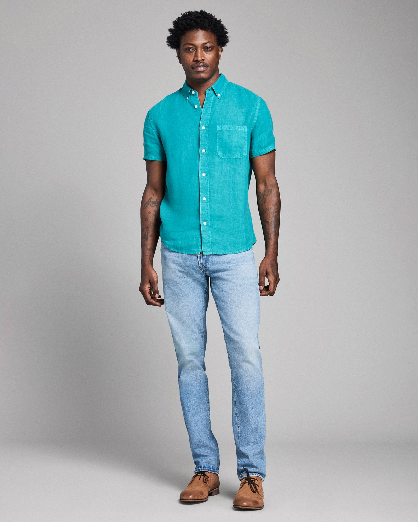 Man wearing a teal button-up shirt and light blue jeans against a gray background