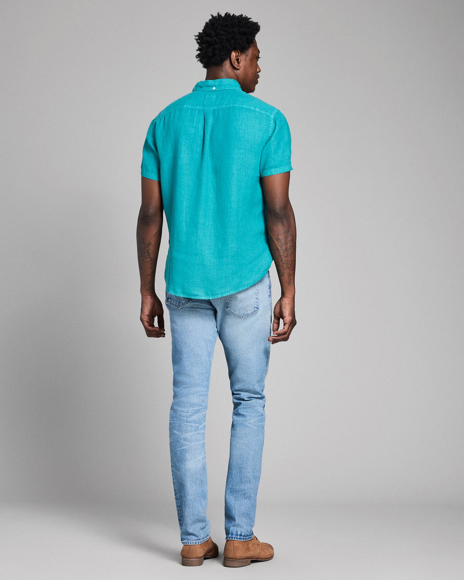 Person wearing a turquoise polo shirt and light blue jeans against a gray background