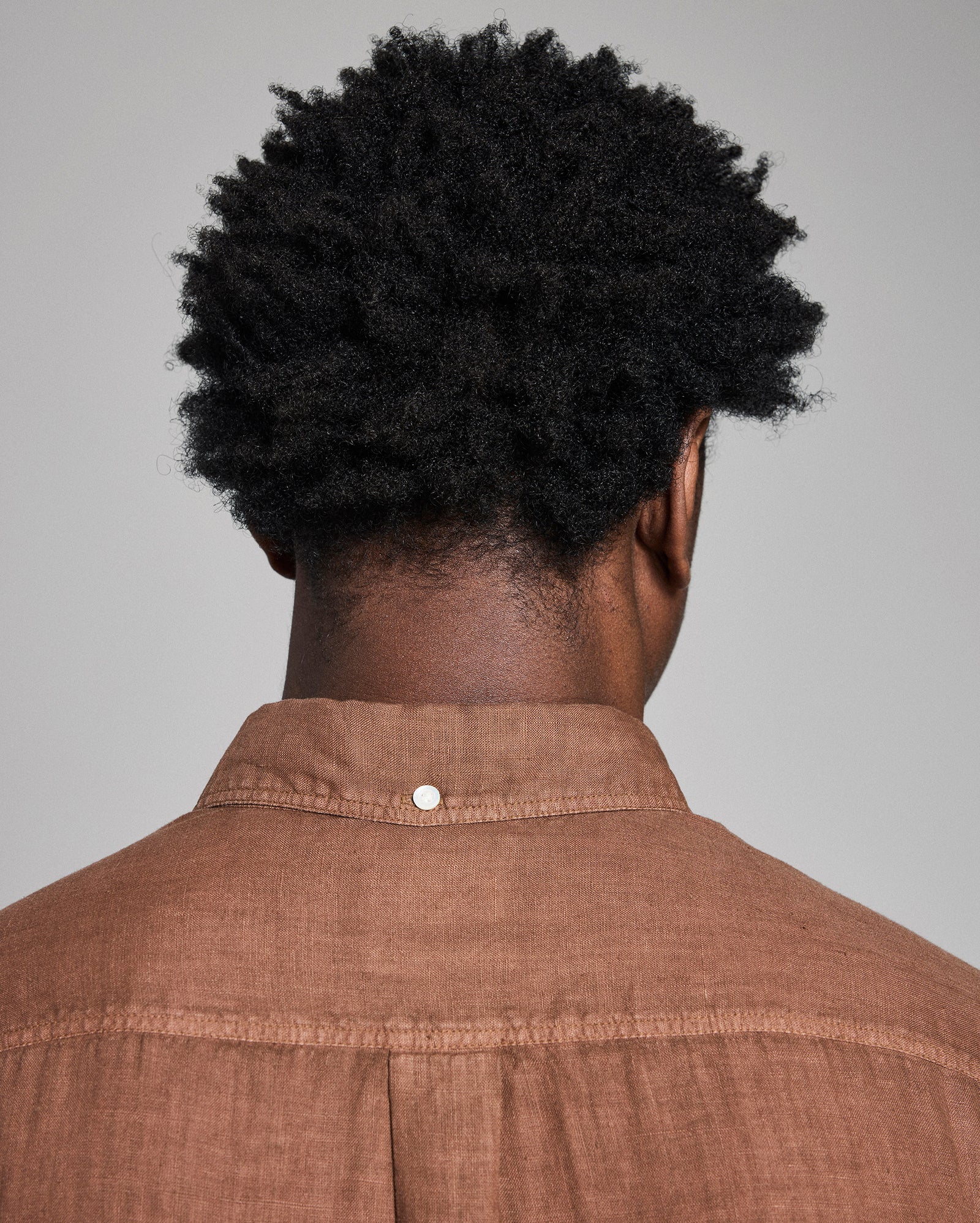 Person wearing a brown shirt with a plain background