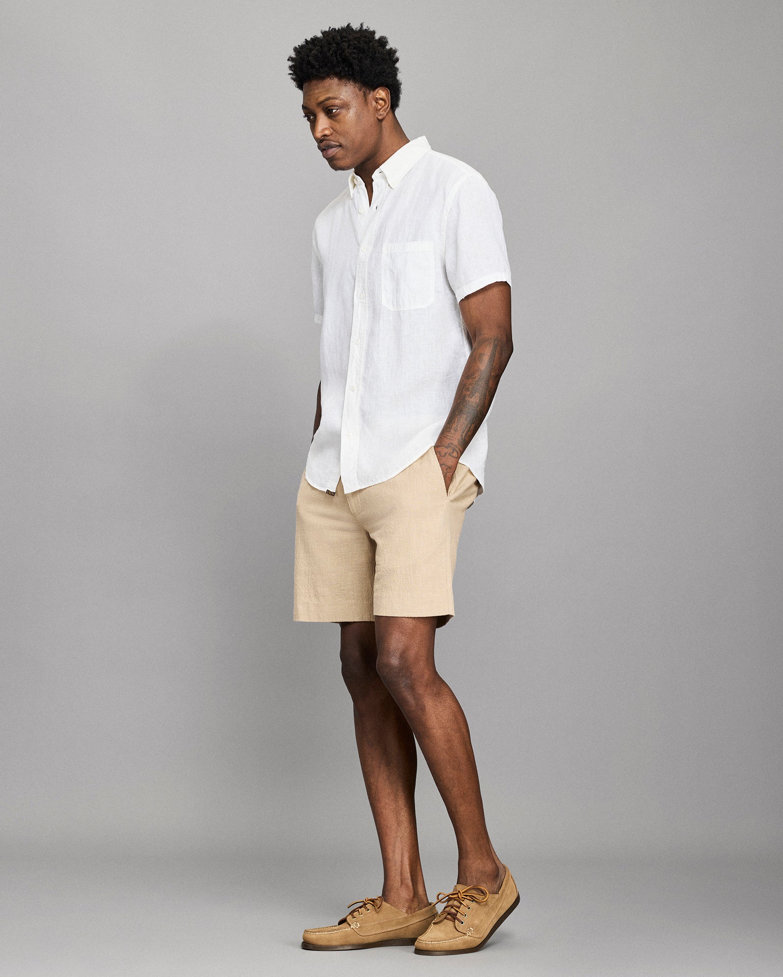 Man wearing a white shirt, beige shorts, and brown shoes on a gray background