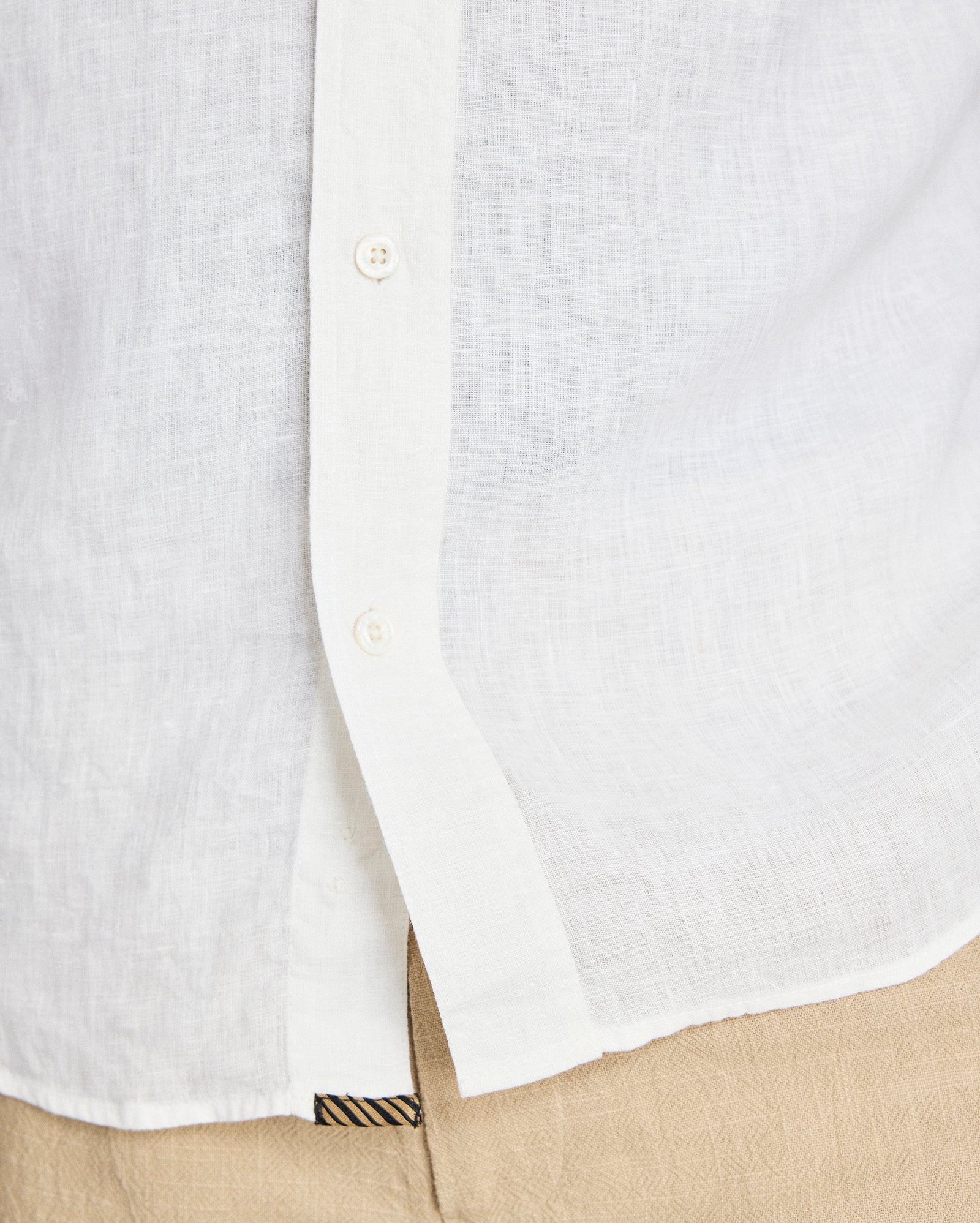 Close-up of a white button-up shirt with a beige pocket and pants.