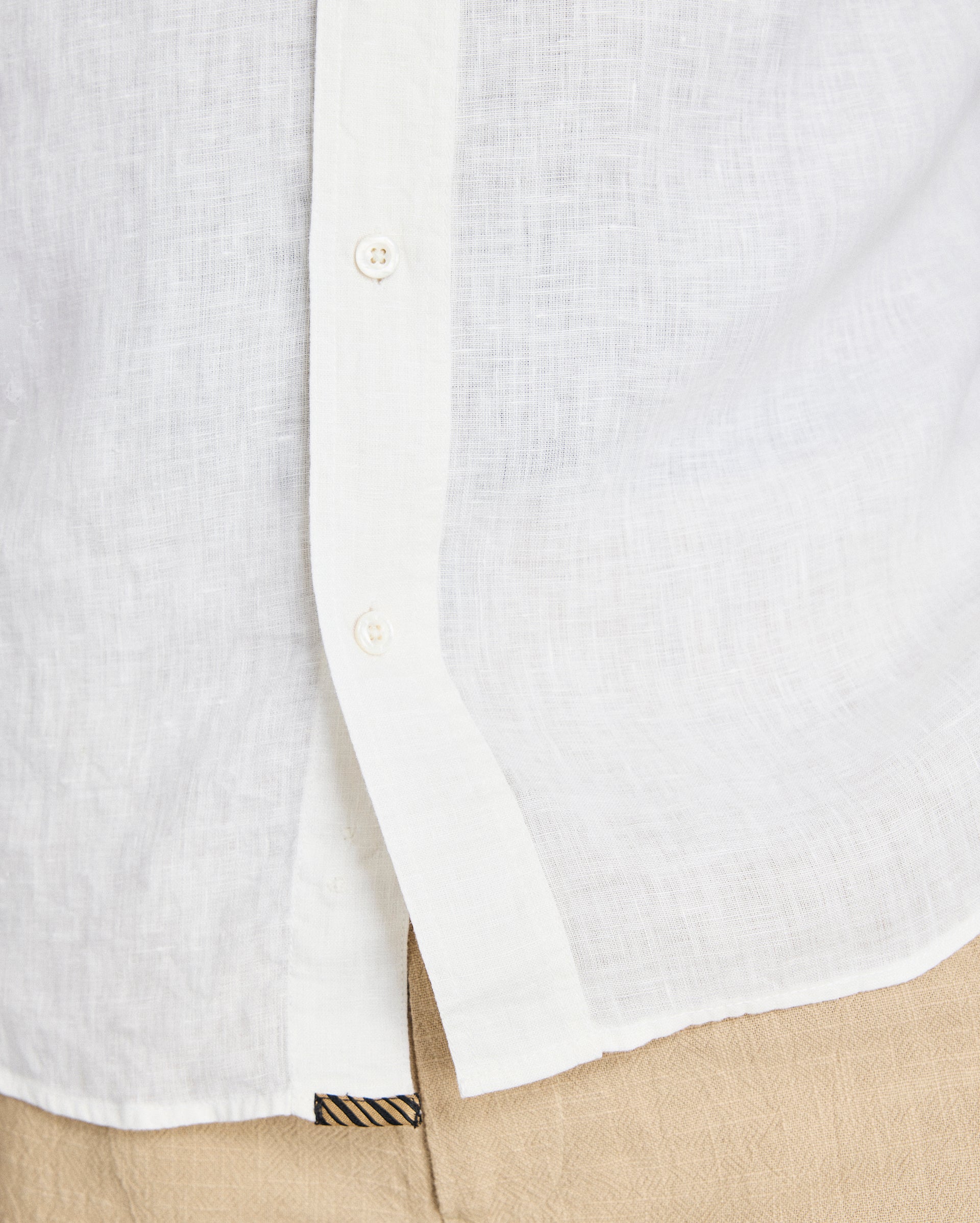 Close-up of a white button-up shirt with a beige pocket and pants.