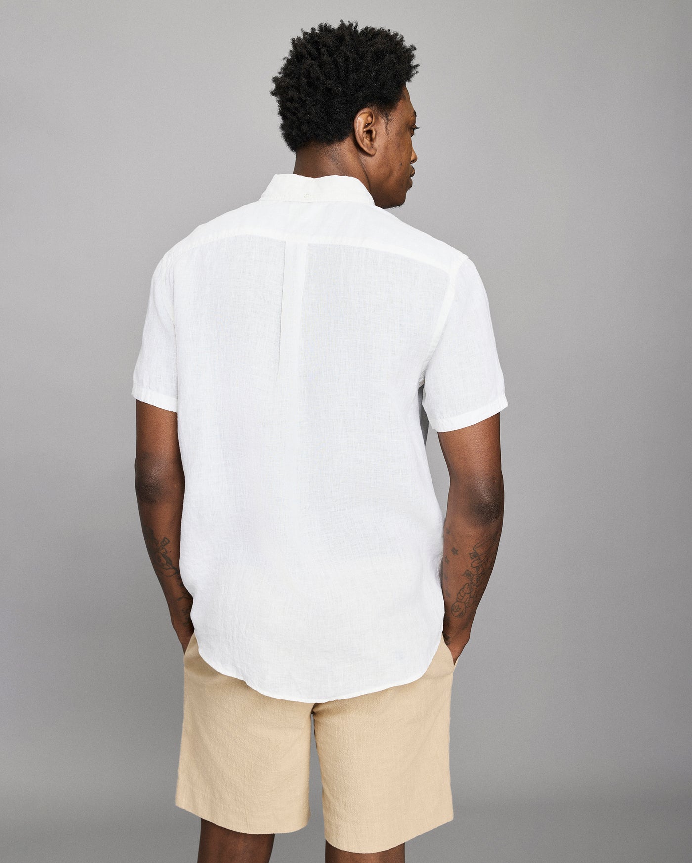 Person wearing a white shirt and beige shorts against a gray background