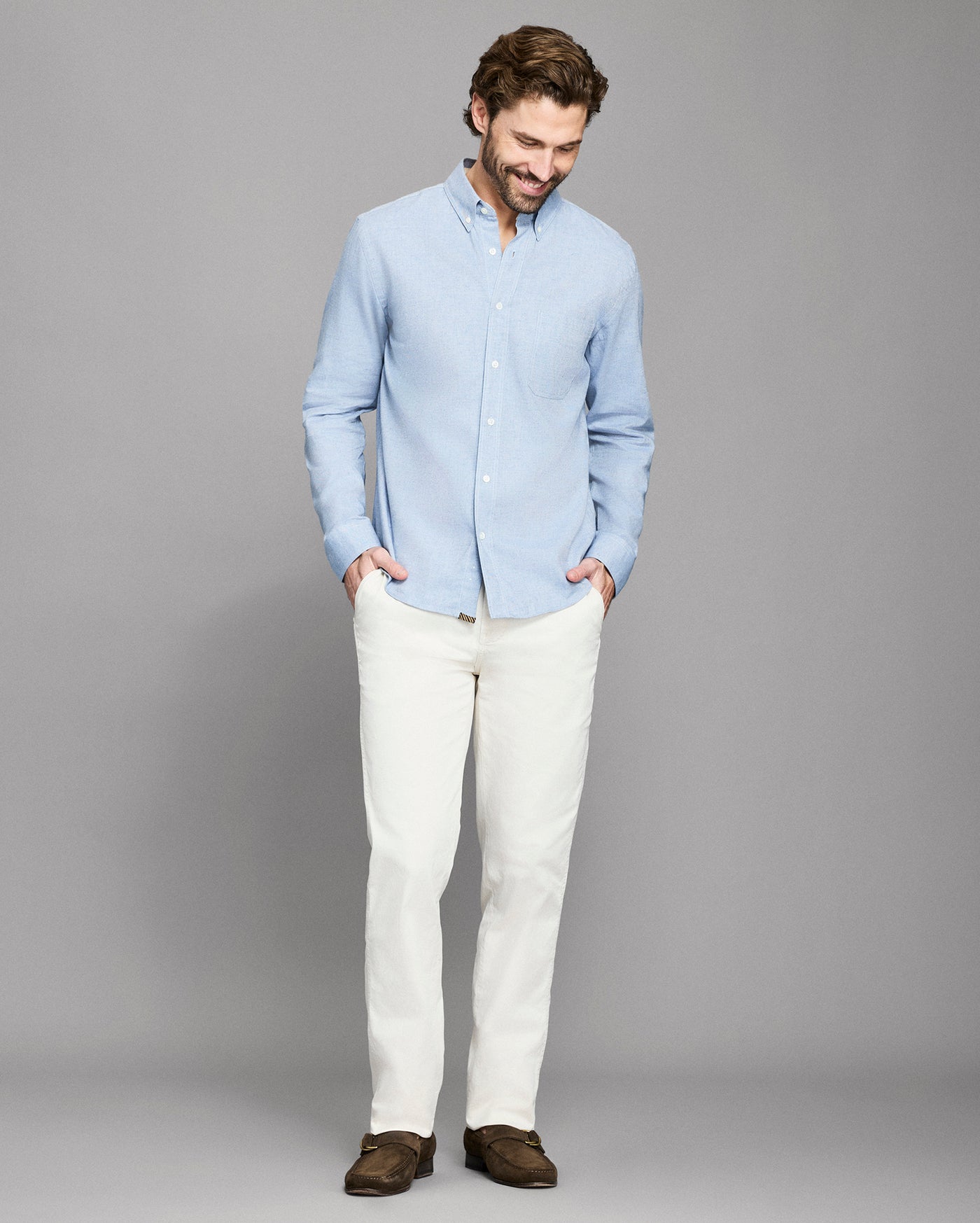 Man wearing a light blue shirt and white pants against a gray background