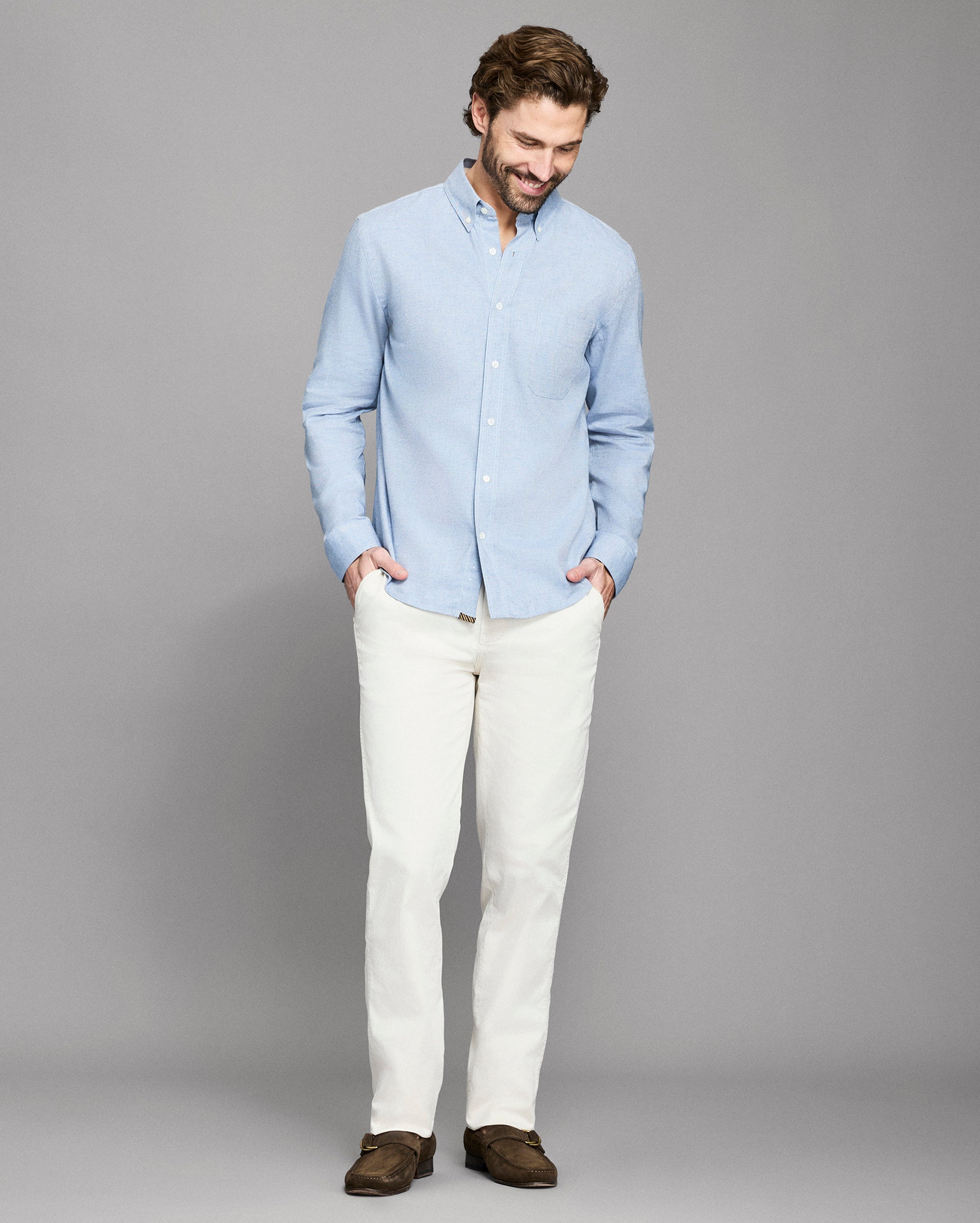 Man wearing a light blue shirt and white pants against a gray background